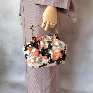 以下が含まれることがあります： 金色の金属製のハンドルが付いた、小さな花柄のハンドバッグ。 バッグは、赤、白、黄色の花柄のデザインが施された黒い背景が特徴です。 ハンドルは、クラスプクロージャーを備えた円形です。