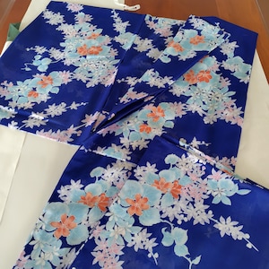 以下が含まれることがあります： 鮮やかなロイヤルブルーの着物で、水色とオレンジの花が繰り返される模様が特徴です。長い袖と伝統的な打ち合わせの構造を持ち、滑らかでサテンのような光沢のある生地で仕上げられています。