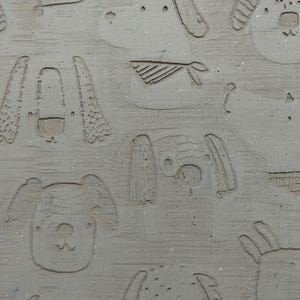 May include: A close-up of a gray, textured surface with an embossed pattern of various dog faces. The dog faces are in different poses and styles, creating a playful and whimsical design.