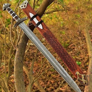 May include: A double-edged steel sword with a dark brown and silver hilt, featuring a matching wooden scabbard adorned with intricate dark brown woven patterns, silver metal accents, and a decorative metal tip at the bottom end of the sheath.