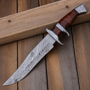 May include: A fixed-blade knife featuring a distinctive wavy Damascus steel pattern on the blade and bolster. The handle is crafted from polished brown wood with a smooth, contoured grip, and the pommel is capped with a matching steel accent.