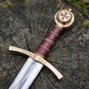 May include: A sword featuring a polished steel blade, a brass crossguard, and a brown leather-wrapped grip accented with gold-coloured wire rings. The circular brass pommel displays a red cross emblem centred on a white circular background.