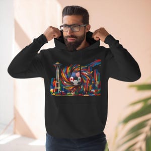 May include: Black hooded sweatshirt featuring a colorful graphic of a soccer ball with flags of different countries, including the USA and Canada, and the Seattle Space Needle. The design is a vibrant mix of colors.