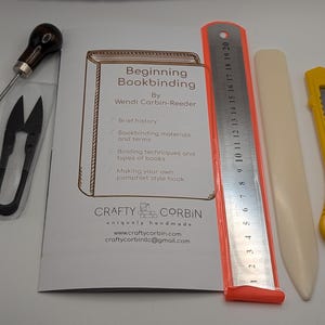May include: A bookbinding kit with tools and a guide. The kit includes a booklet titled "Beginning Bookbinding", a metal ruler, a bone folder, a utility knife, a needle tool, and small scissors.