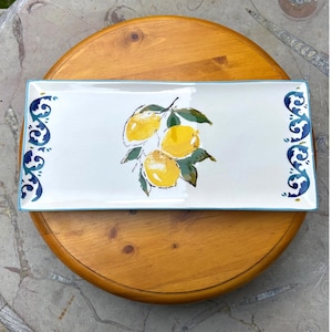May include: Rectangular white ceramic serving platter with a light blue border and decorative blue and white scrollwork on the ends. The centre features a cluster of yellow lemons with green leaves.