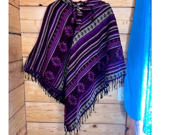 Poncho con cappuccio in lana 100% fatto a mano in Nepal, colore viola, con frange geometriche e chiusura a coulisse.