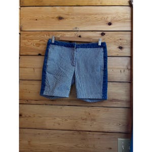May include: Blue and white striped shorts with denim side panels and waistband. The shorts are hanging on a wooden hanger against a wooden background. The shorts have a vertical striped pattern.