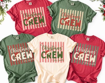 May include: Five short-sleeved crew neck t-shirts in red, green, and cream colors. Each shirt features a graphic with vertical stripes, the text "Christmas CREW" with a Santa hat on the letter C, and the custom text "The Smiths" below.