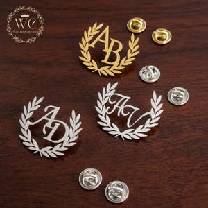 May include: Gold and silver monogram pins with laurel wreath designs. The pins feature initials such as AB, AD, and AV. Several gold and silver pin backs are also visible. The image includes the text "WE Wedding collection".