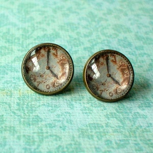 May include: A pair of antique-style clock face earrings with a distressed white background and black hands. The earrings are made of metal with a bronze finish.