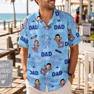 May include: Light blue button-down shirt with a repeating pattern of children's faces, fireworks, and the text "BEST DAD EVER." The shirt has a classic collar and short sleeves, perfect for a summer day. The design incorporates red, white, and blue elements.