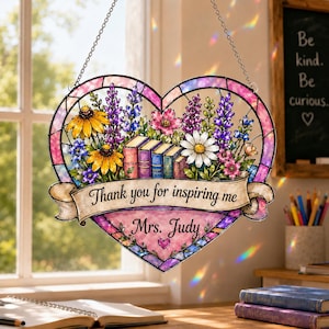 May include: A heart-shaped stained glass suncatcher featuring a colourful floral arrangement with books and a banner that reads Thank you for inspiring me and Mrs. Judy. The design includes yellow, purple, and white flowers with a pink border.
