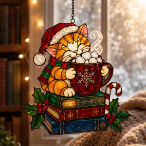 May include: A stained glass ornament featuring a ginger cat wearing a Santa hat and scarf, holding a red mug of marshmallows. The cat sits atop a stack of books with holly and a candy cane.
