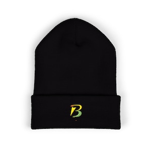 Puede incluir: Gorro negro con borde doblado. El gorro presenta una letra "B" estilizada en amarillo, verde y naranja en la parte delantera. El gorro está hecho de un material de punto suave.