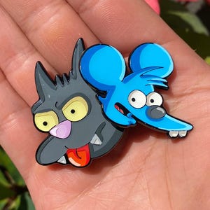 Può includere: Spilla in smalto in stile cartone animato raffigurante un gatto grigio e un topo blu. Il gatto ha occhi gialli, naso rosa e lingua rossa. Il topo ha occhi bianchi, naso grigio e due denti bianchi. Per giacca o borsa.