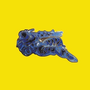 May include: A blue enamel pin with a detailed design, featuring shades of blue and black. The pin is set against a bright yellow background, creating a striking contrast. The design appears to be an abstract creature or form.