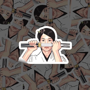 May include: A sticker featuring a stylized illustration of a person holding a katana. The person is depicted with black hair, wearing a white uniform with a black collar. The katana has a black and gold handle and blade.