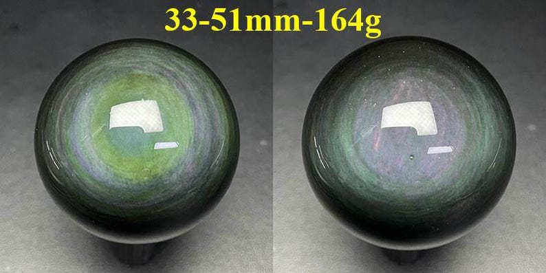 May include: Two polished obsidian spheres, each with a swirling pattern of green, gray, and black. The spheres are approximately 1.3 to 2 inches in diameter and weigh 5.8 ounces. The text "33-51mm-164g" is visible at the top.