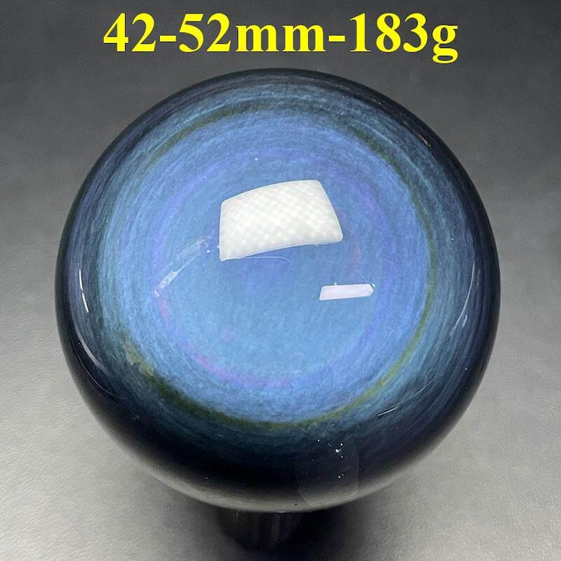 May include: A polished, spherical gemstone with a swirling blue and black pattern. The sphere measures approximately 1.65 to 2.05 inches in diameter and weighs 6.45 ounces. The text "42-52mm-183g" is visible at the top.