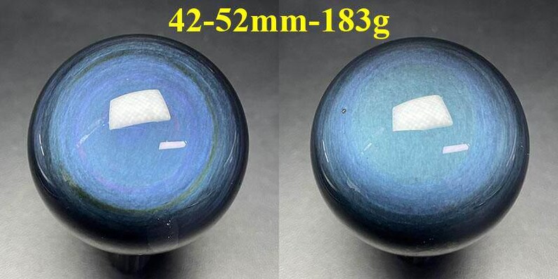 May include: Two polished blue obsidian spheres. The spheres have a reflective surface with a swirling pattern of blue and black. The text "42-52mm-183g" is in the top center.