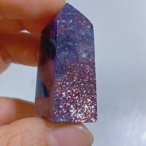Pu&ograve; includere: Un piccolo oggetto in resina di forma esagonale e appuntita, nei toni del viola intenso e del blu. La superficie presenta una densa concentrazione di particelle glitterate multicolori e riflettenti che creano un effetto scintillante.
