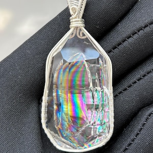 May include: A clear, faceted crystal pendant featuring internal rainbow-colored light refraction, encased in a decorative silver-toned wire-wrapped frame with a matching wire bail at the top for suspension on a necklace chain or cord.