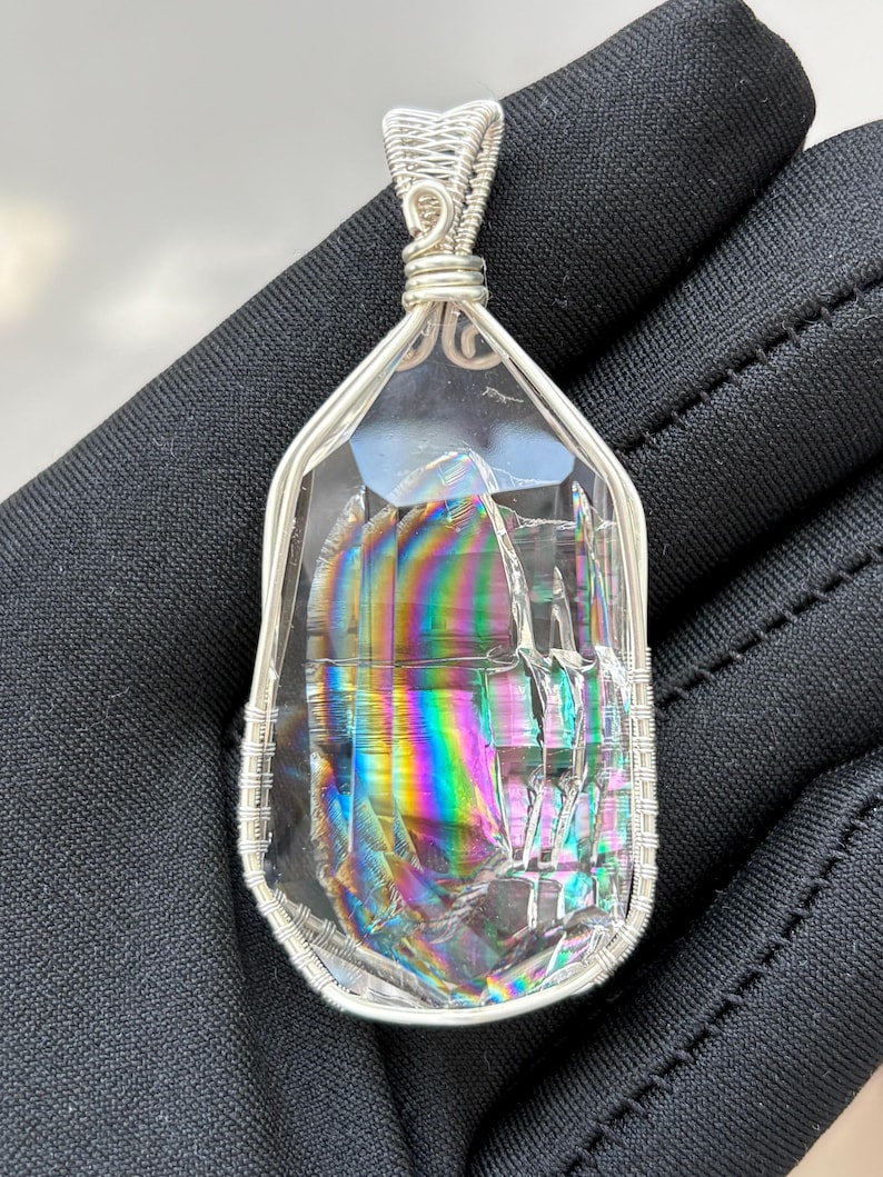 May include: A clear, faceted crystal pendant featuring internal rainbow-colored light refraction, encased in a decorative silver-toned wire-wrapped frame with a matching wire bail at the top for suspension on a necklace chain or cord.