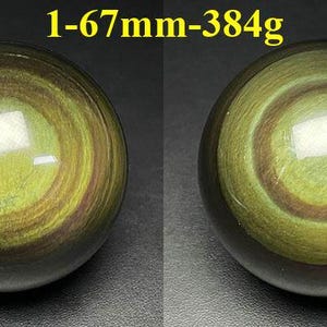 May include: Two polished obsidian spheres, each with concentric rings of olive green and brown hues. The spheres are approximately 2.6 inches in diameter and weigh 13.5 ounces. The text "1-67mm-384g" is visible above the spheres.