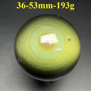 May include: A polished, spherical gemstone with concentric bands of green and yellow hues. The stone has a weight of 193g and a diameter between 36-53mm. A white, rectangular inclusion is visible on the surface.