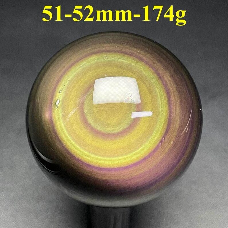 May include: A polished, spherical gemstone with a swirling pattern of yellow, purple, and brown hues. The sphere measures 51-52mm in diameter and weighs 174g. The text "51-52mm-174g" is displayed at the top of the image.