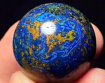 May include: A polished spherical stone featuring a vibrant mix of deep royal blue, bright turquoise, and metallic gold mineral inclusions. The surface displays a swirling, marbled pattern with a high-gloss finish that reflects light.