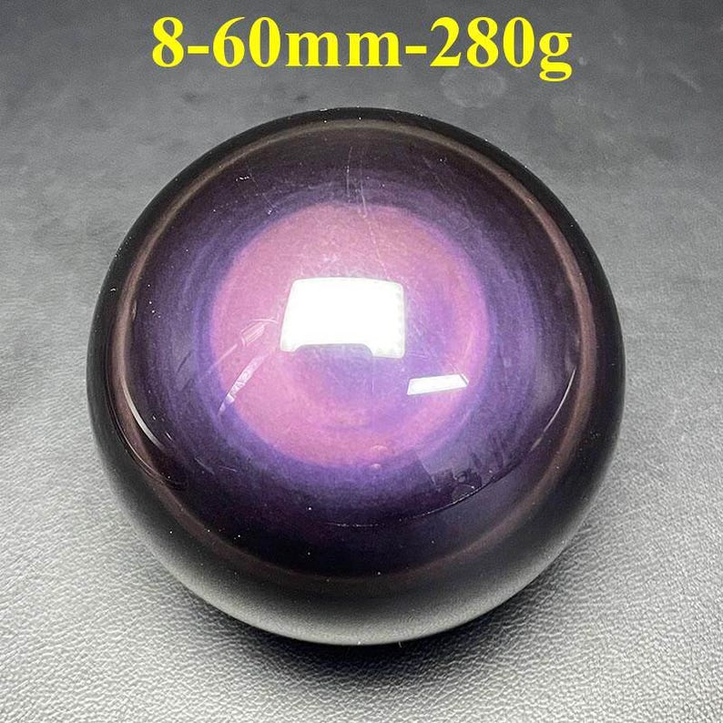May include: A polished, spherical gemstone with a swirling pattern of purple and black. The text "8-60mm-280g" is visible at the top. The sphere has a glossy finish and reflects light.