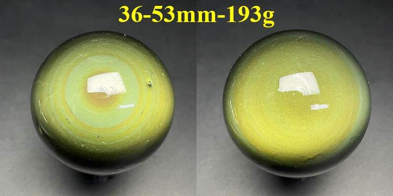 May include: Two polished, spherical gemstones with a swirling pattern of green and yellow hues. The text above the spheres reads "36-53mm-193g". The spheres have a reflective surface.