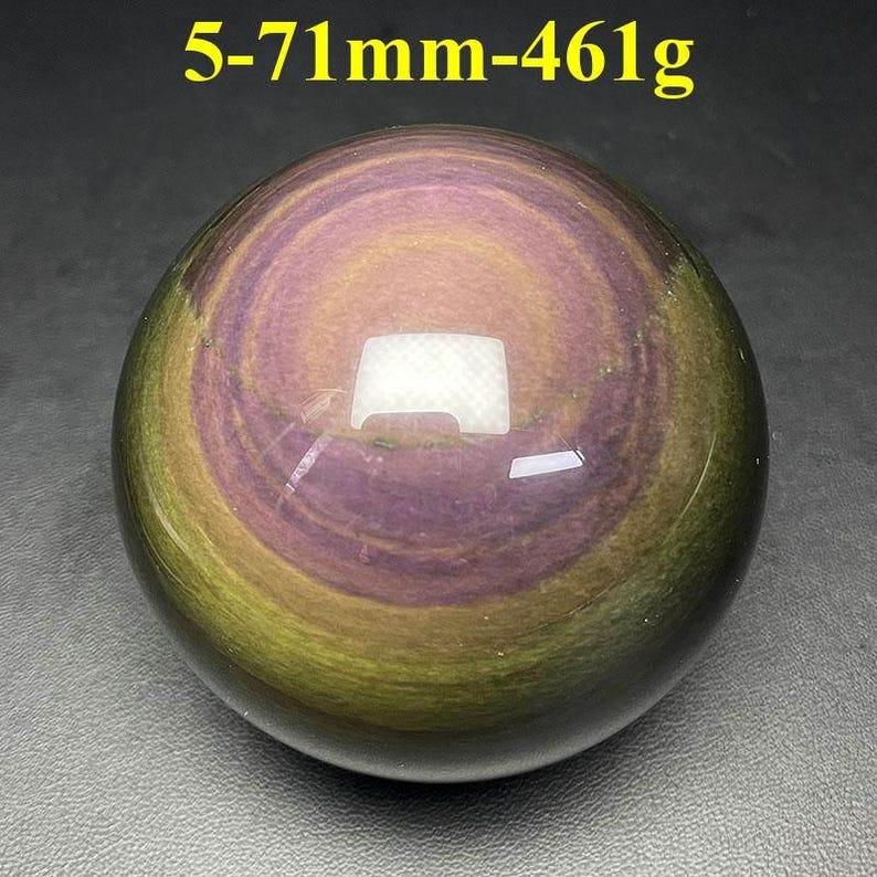 May include: A polished, spherical gemstone with a swirling pattern of purple, gold, and green hues. The stone measures approximately 2.8 inches in diameter and weighs 16.3 ounces. The text "5-71mm-461g" is visible at the top.