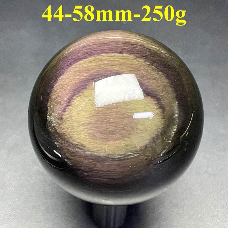 May include: A polished, spherical gemstone with a swirling pattern of purple, gold, and black. The sphere measures between 1.73 to 2.28 inches in diameter and weighs 8.8 ounces. The text "44-58mm-250g" is visible at the top.
