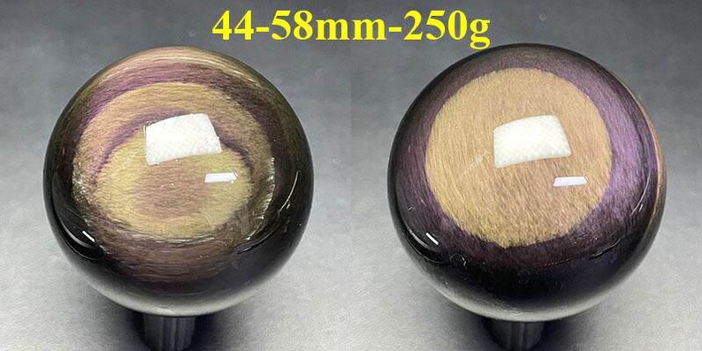 May include: Two polished obsidian spheres, each with a swirling pattern of gold, purple, and black. The spheres are approximately 1.7 to 2.3 inches in diameter and weigh 8.8 ounces. The text "44-58mm-250g" is visible above the spheres.