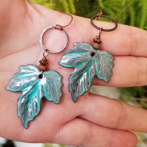 May include: A pair of dangle earrings featuring teal green ceramic leaves with copper wire accents and brown beads.