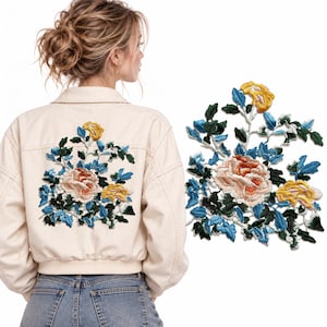 Può includere: Una toppa floreale ricamata con una grande rosa centrale color pesca, fiori gialli più piccoli e intricate foglie blu e verde scuro. La toppa è mostrata applicata sul retro di una giacca color crema e come articolo a sé stante.