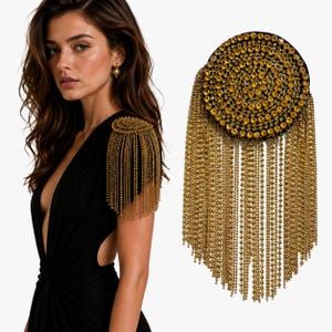 May include: A circular shoulder epaulette featuring a dense arrangement of sparkling yellow crystals set against a black base, adorned with long, cascading gold-toned metal chains that drape downwards to create a shimmering, textured fringe effect.