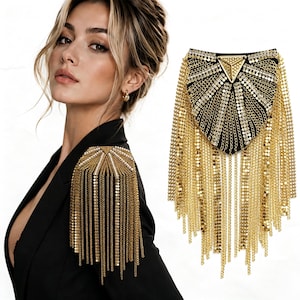 May include: A gold-tone shoulder epaulet featuring a triangular metal centerpiece, radiating rows of sparkling rhinestones, and long dangling metallic chains. The accessory is mounted on a black fabric base with a structured, fan-like design.
