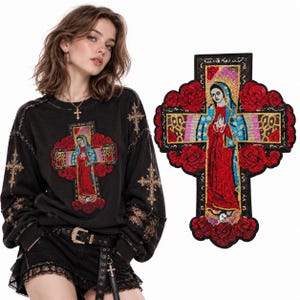 Pode incluir: Uma camisola preta de manga comprida com um grande emblema de lantejoulas coloridas de uma figura com túnica vermelha e azul sobre uma cruz rodeada de rosas vermelhas. A camisola inclui também pequenos emblemas de cruz nas mangas.