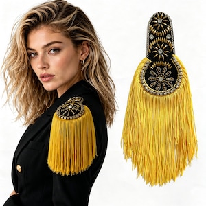 May include: A black shoulder epaulet featuring intricate gold beadwork, metallic accents, and a central floral-inspired design, finished with long, flowing yellow fringe that hangs down from the base of the decorative piece.