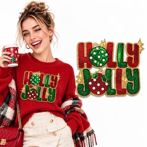 Puede incluir: Un suéter rojo de manga larga con un gráfico de lentejuelas que dice HOLLY JOLLY en letras rojas y verdes, con dos adornos circulares integrados en el diseño del texto. El suéter tiene cuello redondo y puños acanalados.