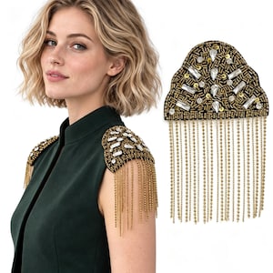 May include: A pair of black shoulder epaulets featuring gold beadwork, sequins, and clear crystal accents. Each piece has a curved top edge and a long fringe of delicate gold chains hanging from the bottom, designed to be worn on the shoulders.