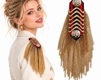 Puede incluir: Una hombrera con una base de tela negra y roja con detalles de chevrón en tono dorado, dos botones metálicos en tono plateado y largas cadenas de metal dorado en cascada que cuelgan de los lados de la estructura rectangular.
