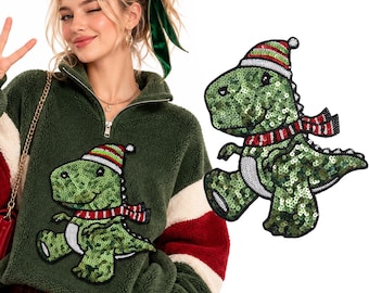 Puede incluir: Un suéter de forro polar verde oscuro con cremallera corta y un parche de dinosaurio de lentejuelas. El dinosaurio es verde con vientre blanco, lleva un gorro de invierno y una bufanda a rayas rojas, blancas y verdes. El parche se muestra por separado.
