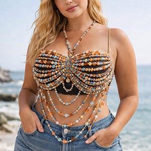 May include: A beaded top with a halter neck and multiple strands of beads cascading down the torso. The top features a mix of orange, blue, and brown beads. The model is wearing denim shorts.