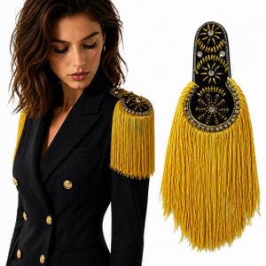 May include: A black shoulder epaulette featuring gold-toned fringe, intricate beadwork, and clear crystal accents. The piece is designed with a rounded top and a U-shaped base, showcasing a floral-inspired pattern of beads and metallic embellishments.
