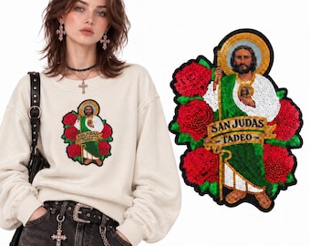 Puede incluir: Una sudadera beige de manga larga con un gran parche de lentejuelas de colores de San Judas Tadeo. El parche muestra la figura con una túnica verde y blanca rodeada de rosas rojas, con el texto SAN JUDAS TADEO en una pancarta dorada.