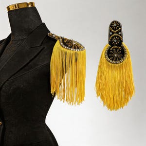 May include: A black blazer with a gold trim and a decorative shoulder epaulet. The epaulet features a black base with gold and silver embellishments and long yellow fringe.